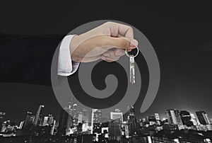 Hand holding keys with city background, real estate and property concept