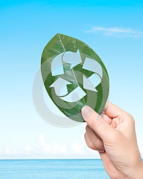 Hand holding leaf with hole of recycling symbol, resource recovery