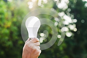 hand holding led bulb on green nature background and sunshine.