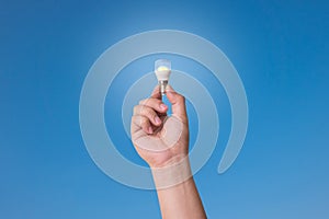 Hand holding LED Bulb with Lighting on blue sky background.