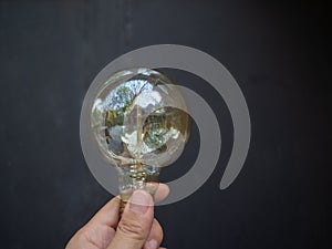 A hand is holding a light bulb against a dark background. The lightbulb represents idea and innovation concept