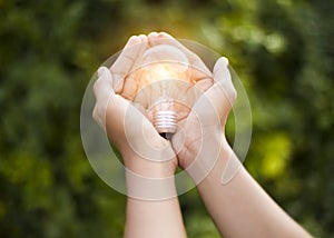 Hand holding light bulb against nature, icons energy sources for renewable,