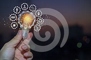 Hand holding light bulb against nature with icons energy sources for renewable