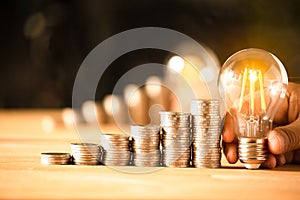 Hand holding a light bulb with coins stack