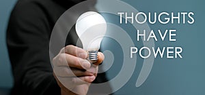 Hand holding light bulb with text Thoughts Have Power.