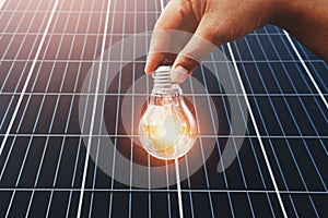 hand holding lightbulb with solar panel background. clean energy in nature concept