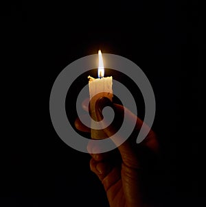 A hand holding a lighted candle in the dark. The light of a burning candle in a dark room. A candle on a black background