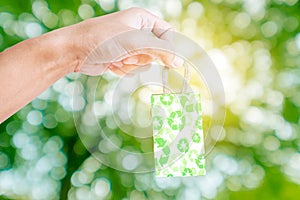 Hand holding little packet green recycle paper bag, on green Bokeh and bright yellow light background