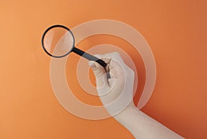 Hand holding a magnifier against color background