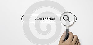 Hand holding magnifier glass with 2024 trends searching bar for optimization 2024 business marketing trends and planing change