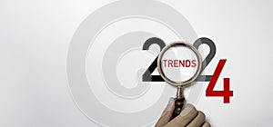 Hand holding magnifier glass with 2024 year and trends wording for focusing 2024 business marketing trends and planing change