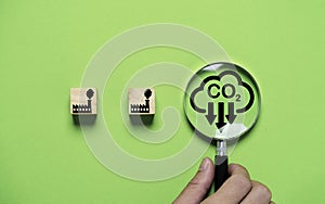 Hand holding magnifier glass with CO2 reducing icon and black factory for decrease CO2 emission, carbon footprint and carbon