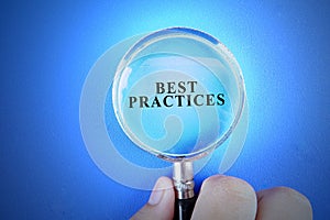 Hand holding magnify glass over a blue background with BEST PRACTICES words. photo