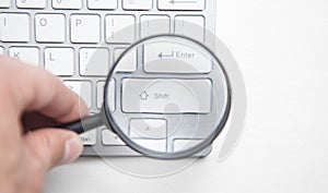 Hand holding magnifying glass with computer keyboard
