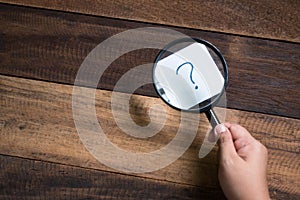 Hand holding magnifying glass focusing on question mark