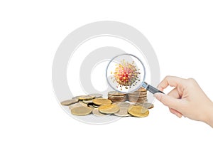 Hand holding magnifying glass and inspecting stacked coins.