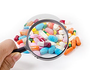 Hand holding magnifying glass with medicine pills.