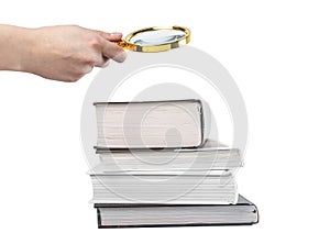 Hand holding magnifying glass over books stack isolated on white background. Research and detailed study of information