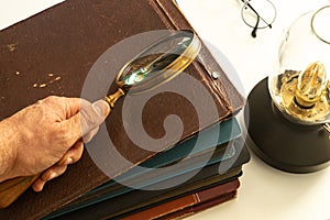 Hand holding a magnifying glass over old photo albums, Luminous vintage lamp, Concept of memories and historical and family