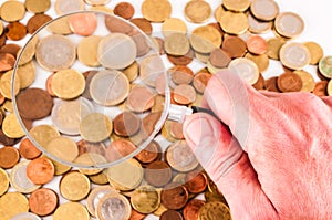 A hand holding a magnifying glass over a pile of coins