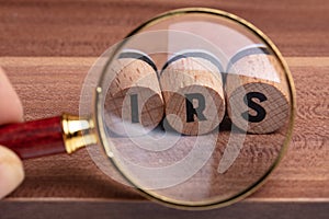 Hand Holding Magnifying Glass Over Wooden Cork With IRS Text