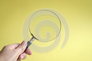 Hand holding magnifying glass. On yellow background