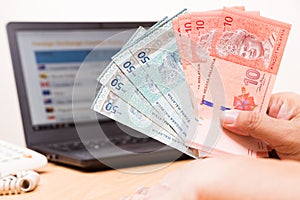 Hand holding Malaysia Ringgit in office with computer in background