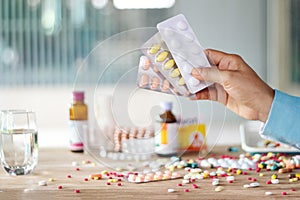 Hand holding medicines pill pack with colorful drugs spread on photo