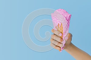 Hand Holding a Melting Pink Ice Cream Cone Against a Blue Background