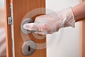 Hand holding metal door handle in white rubber glove - virus spread prevention concept