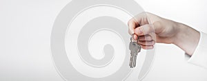 Hand holding metal keys on keyring in fingers over white gray background. Ad banner for real estate with copy space for