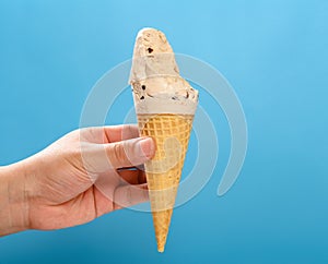 hand holding milk tea flavor ice cream cone with couple of bites on a blue background horizontal composition