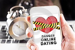 Hand holding mobile with caution tape on heart and Danger online