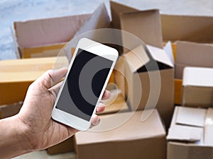 Hand holding mobile over blurry background of used deliverly brown corrugated cardboard box