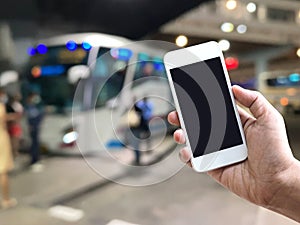 hand holding mobile phone over blur background of bus platform at night