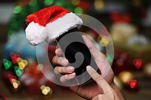 Hand holding mobile phone with Santa Claus ` hat on top on Christmas