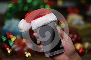 Hand holding mobile phone with Santa Claus ` hat on top on Christmas