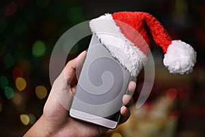 Hand holding mobile phone with Santa Claus ` hat on top on Christmas