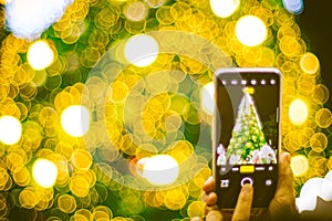 Hand holding mobile smart phone with Christmas light decorated background