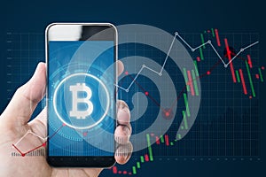 Hand holding mobile smartphone with B symbol of Bitcoin, internet banking and block chain on screen and raising graph background