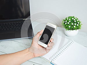 Hand holding mobilephone with workspace on white wood table background