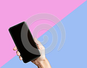 Hand holding mock up smart phone on pink and blue background.
