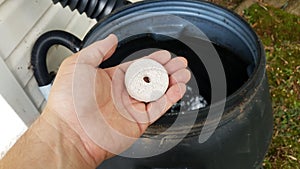 Hand holding mosquito tablet insecticide over rain barrel