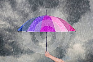 Hand holding multicolored umbrella under dark sky with rain