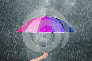 Hand holding multicolored umbrella under dark sky with rain