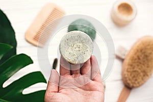 Hand holding natural solid shampoo bar on background of bamboo b