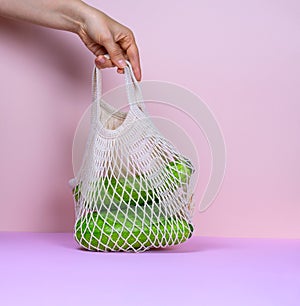 hand holding net bag full of fresh organic vegetables on a pink background