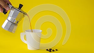 The Hand holding old maker tool, machine of moka pot coffee pouring into white cup on yellow paper background. Copy space for your