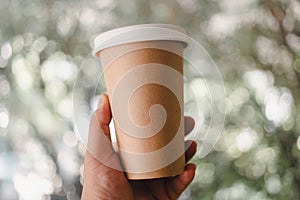 Hand holding one brown coffee paper cup with a lid