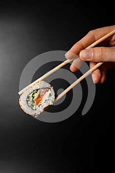 hand holding one piece of roll california with smoked salmon garnished sesame seeds with bamboo chopsticks